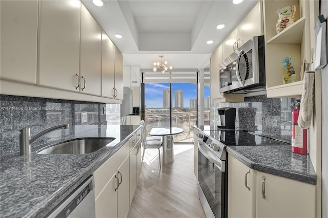 kitchen with an inviting chandelier, a raised ceiling, sink, decorative backsplash, and stainless steel appliances