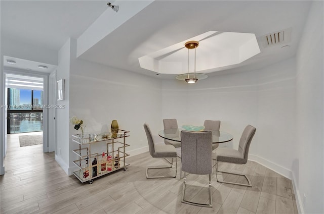 dining area with a raised ceiling and light hardwood / wood-style flooring