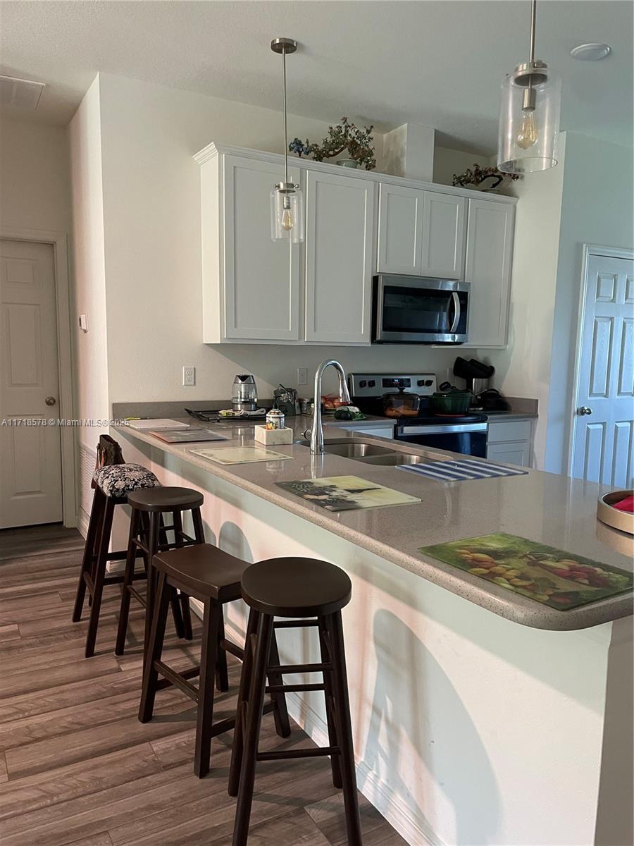 kitchen with white cabinetry, hardwood / wood-style floors, decorative light fixtures, a breakfast bar area, and appliances with stainless steel finishes