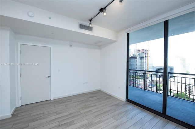 unfurnished room with light wood-type flooring, track lighting, expansive windows, and a healthy amount of sunlight