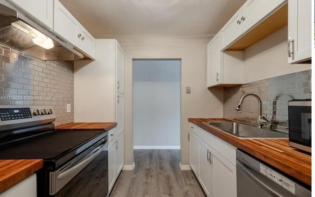 kitchen with wood counters, stainless steel appliances, white cabinets, and sink