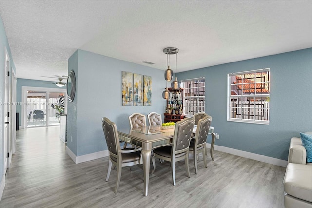 dining space with ceiling fan, light wood-type flooring, and a textured ceiling