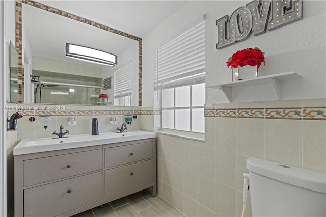 bathroom featuring vanity, toilet, a shower with shower door, and tile walls