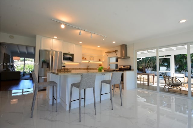 kitchen with light stone countertops, a breakfast bar, stainless steel appliances, wall chimney range hood, and white cabinets