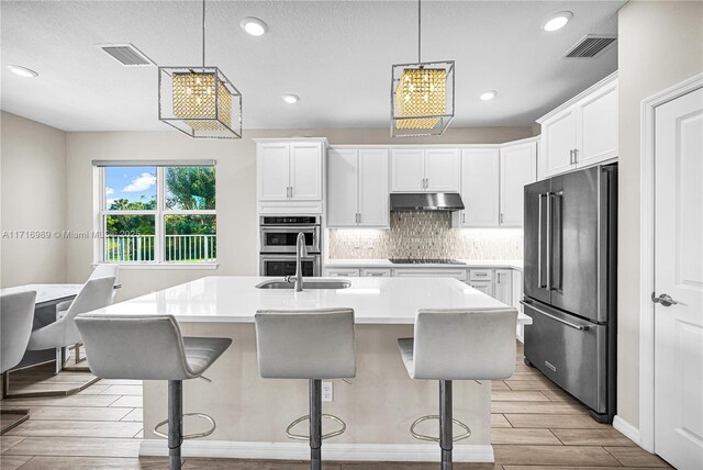 kitchen with white cabinetry, a center island with sink, a kitchen breakfast bar, pendant lighting, and stainless steel appliances