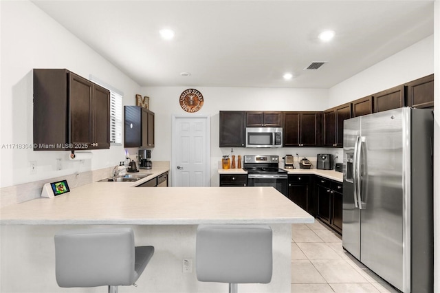 kitchen with kitchen peninsula, stainless steel appliances, sink, a breakfast bar area, and light tile patterned flooring