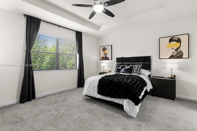 bedroom featuring a raised ceiling, ceiling fan, and light carpet