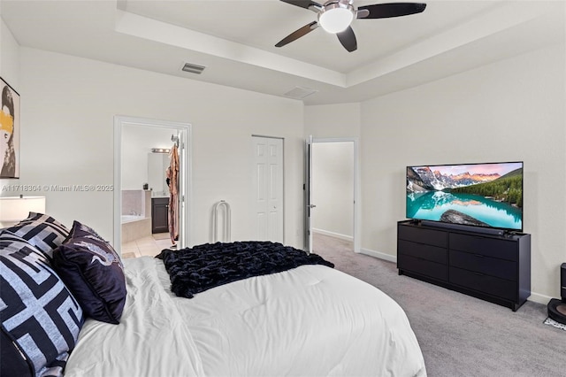 bedroom featuring ceiling fan, a raised ceiling, light colored carpet, and connected bathroom