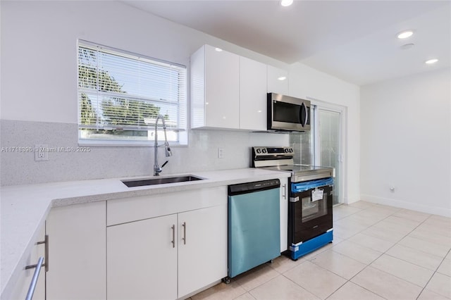 kitchen featuring sink, decorative backsplash, light tile patterned floors, appliances with stainless steel finishes, and white cabinetry