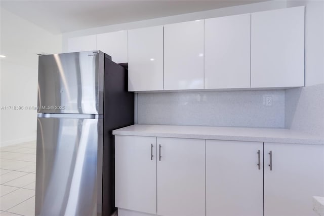 kitchen with light tile patterned floors, backsplash, white cabinetry, and stainless steel refrigerator