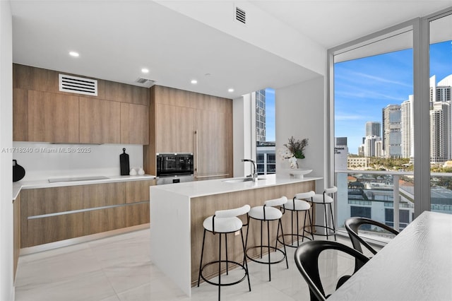 kitchen with black appliances, expansive windows, sink, and a breakfast bar area