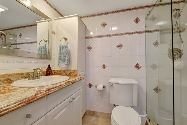 bathroom with a tile shower, tile patterned floors, toilet, vanity, and tile walls