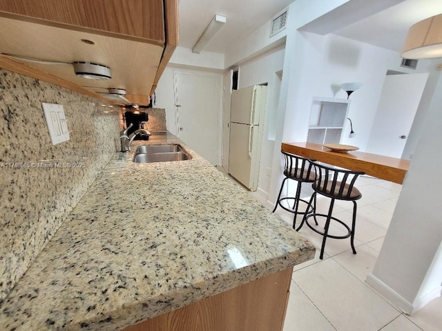 kitchen featuring light stone countertops, sink, white refrigerator, decorative backsplash, and light tile patterned floors