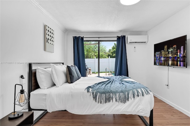 bedroom with hardwood / wood-style floors, a wall mounted air conditioner, access to exterior, crown molding, and a textured ceiling