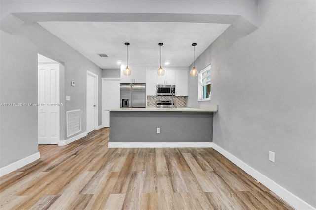 kitchen featuring stainless steel appliances, white cabinets, decorative backsplash, kitchen peninsula, and light wood-type flooring