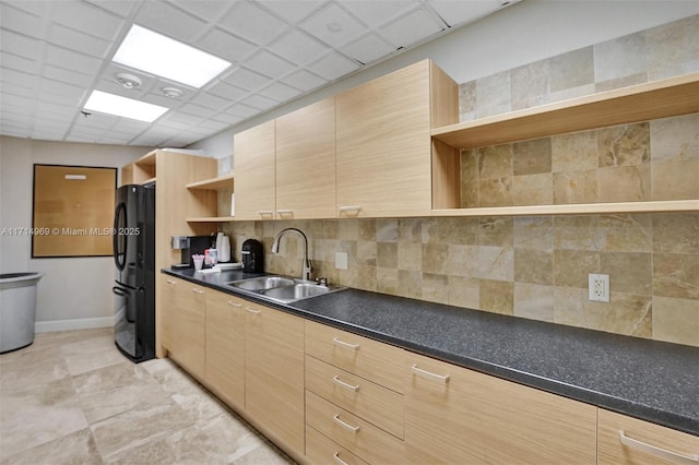 kitchen with tasteful backsplash, a paneled ceiling, black refrigerator, and sink