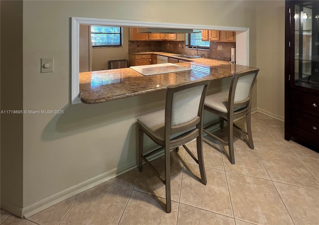 bar with backsplash, stone counters, white dishwasher, sink, and light tile patterned floors