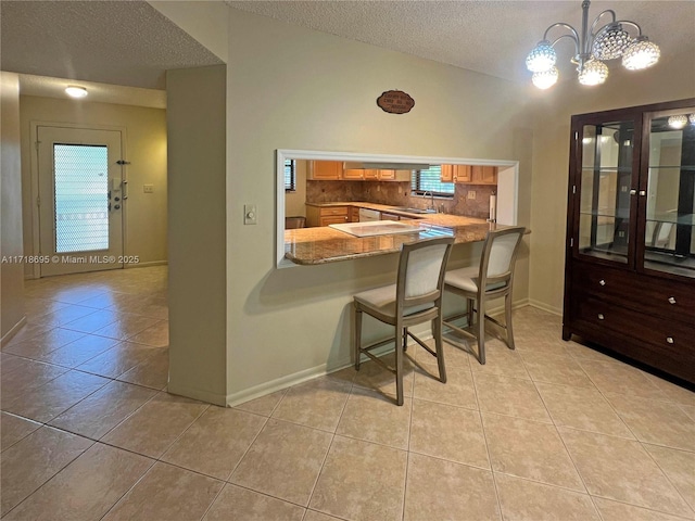 kitchen featuring a kitchen breakfast bar, kitchen peninsula, a textured ceiling, decorative light fixtures, and light tile patterned flooring