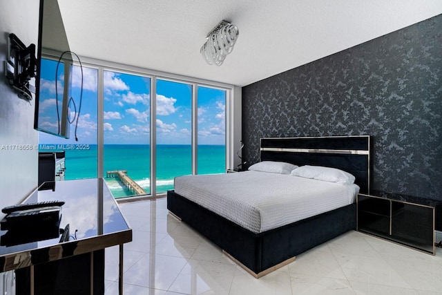 bedroom featuring access to exterior, a textured ceiling, a water view, and expansive windows