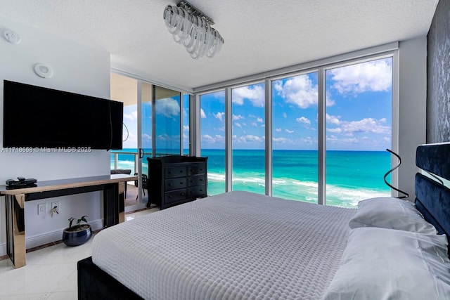 bedroom with access to exterior, a water view, a textured ceiling, and a wall of windows