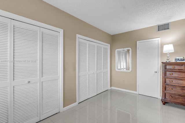 unfurnished bedroom featuring light tile patterned flooring, a textured ceiling, and two closets