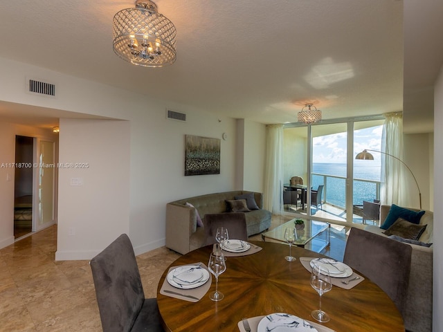 dining room with a textured ceiling, a water view, an inviting chandelier, and floor to ceiling windows