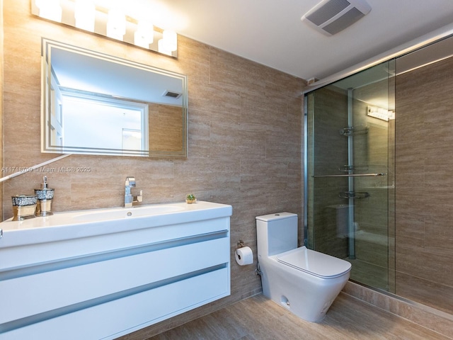 bathroom featuring vanity, toilet, a shower with door, and tile walls