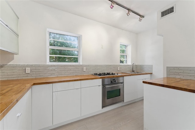 kitchen featuring appliances with stainless steel finishes, rail lighting, tasteful backsplash, white cabinetry, and butcher block counters