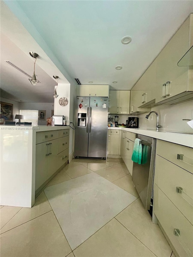 kitchen with stainless steel appliances, light tile patterned floors, cream cabinetry, and decorative light fixtures