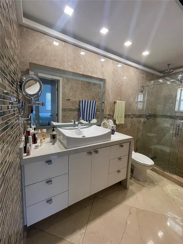 bathroom with vanity, toilet, a shower with door, and tile walls