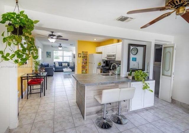 kitchen with a breakfast bar, white refrigerator, a center island with sink, and white cabinetry