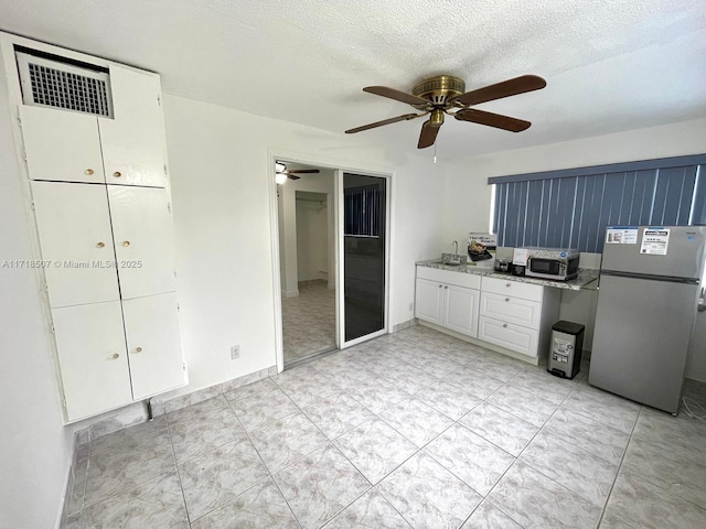 kitchen with sink, ceiling fan, stainless steel fridge, a textured ceiling, and white cabinetry