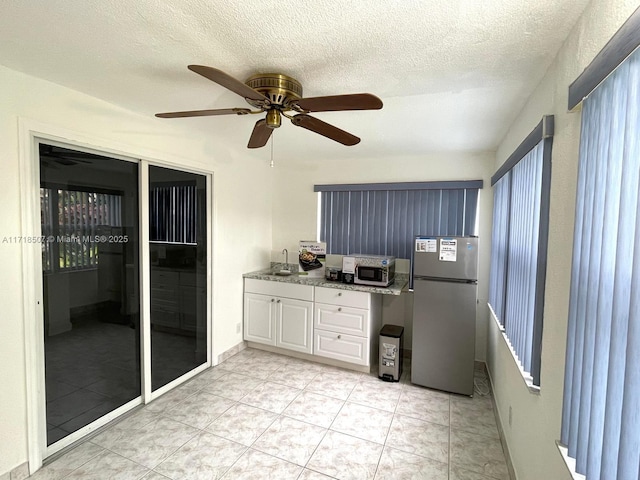 kitchen featuring ceiling fan, sink, stainless steel fridge, a textured ceiling, and white cabinets