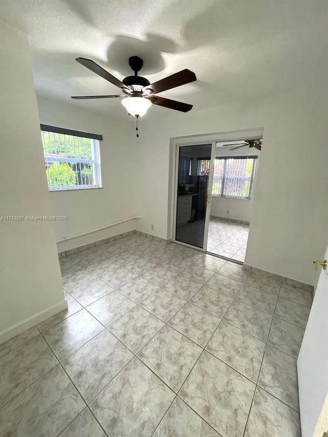 unfurnished room with ceiling fan, light tile patterned flooring, and a textured ceiling