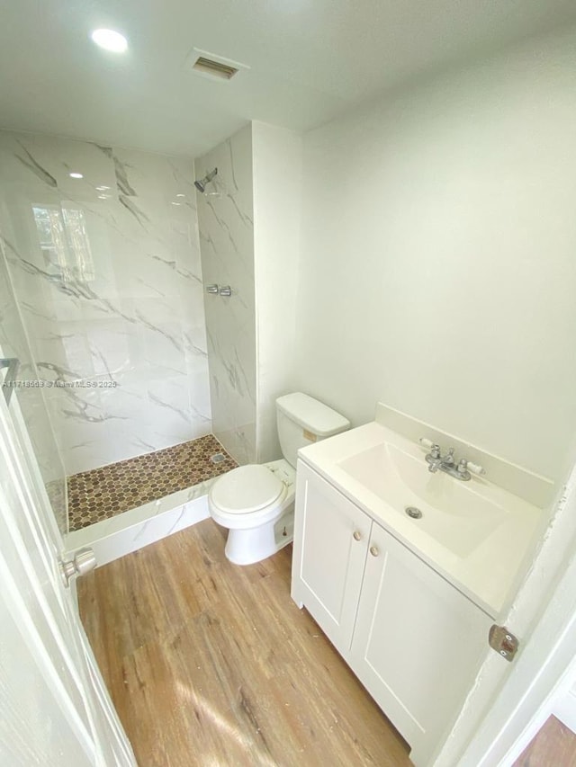 bathroom with wood-type flooring, vanity, a tile shower, and toilet