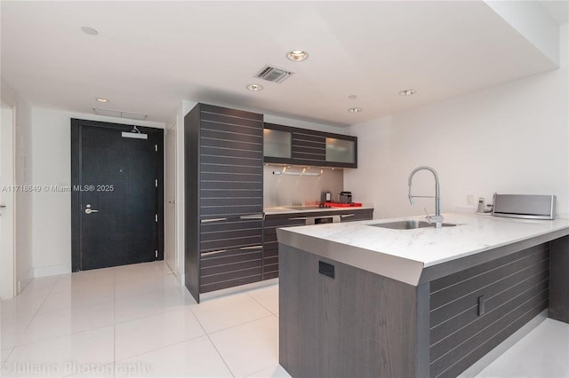 kitchen featuring light tile patterned floors, cooktop, light stone counters, and sink