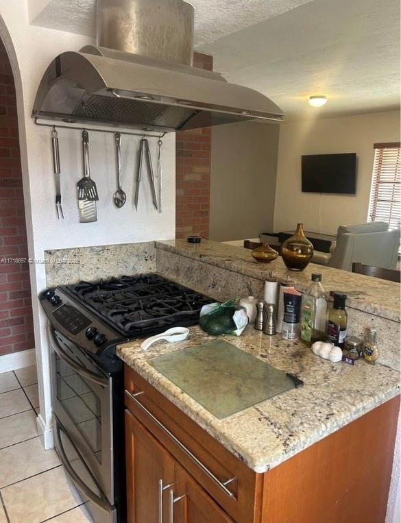 kitchen featuring stainless steel range with gas cooktop, light tile patterned floors, light stone counters, and ventilation hood