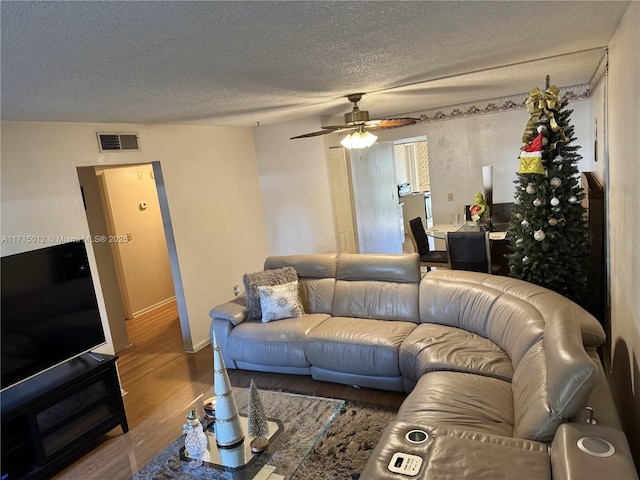 living room featuring hardwood / wood-style flooring, ceiling fan, and a textured ceiling