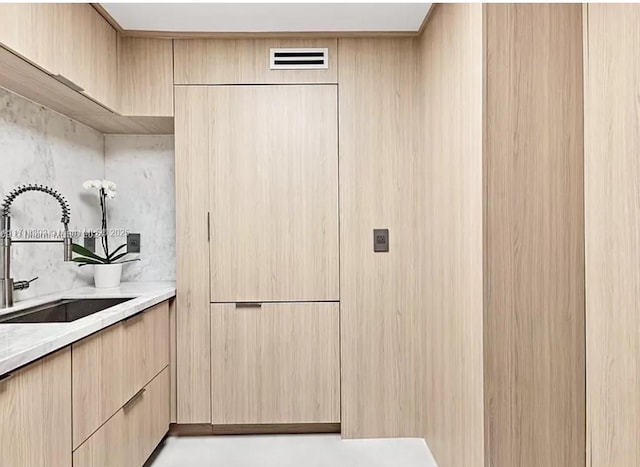 kitchen featuring tasteful backsplash, light stone counters, light brown cabinetry, and sink