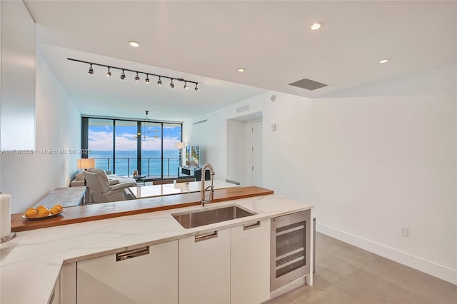 kitchen featuring white cabinetry, sink, wine cooler, light stone counters, and a water view