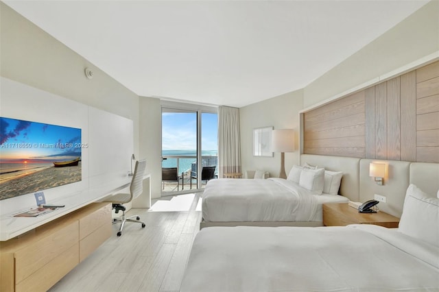 bedroom featuring floor to ceiling windows, a water view, light wood-type flooring, and access to exterior