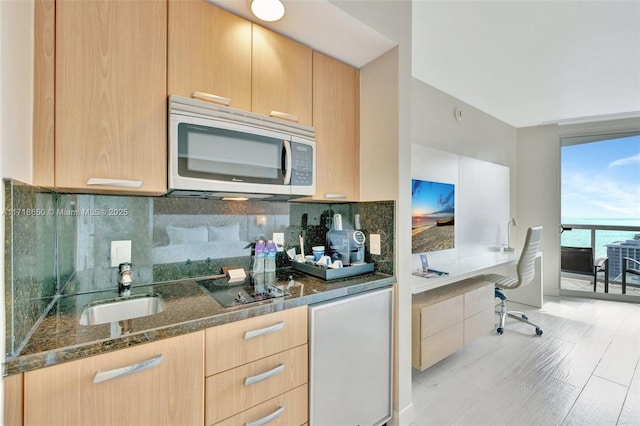 kitchen featuring sink, light brown cabinets, cooktop, dark stone counters, and a water view