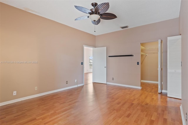 unfurnished bedroom with light wood-type flooring, a walk in closet, a closet, and ceiling fan