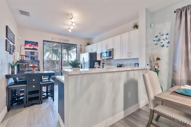 kitchen featuring stainless steel appliances, kitchen peninsula, light hardwood / wood-style flooring, and white cabinets