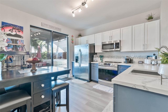 kitchen with sink, light wood-type flooring, white cabinets, stainless steel appliances, and backsplash