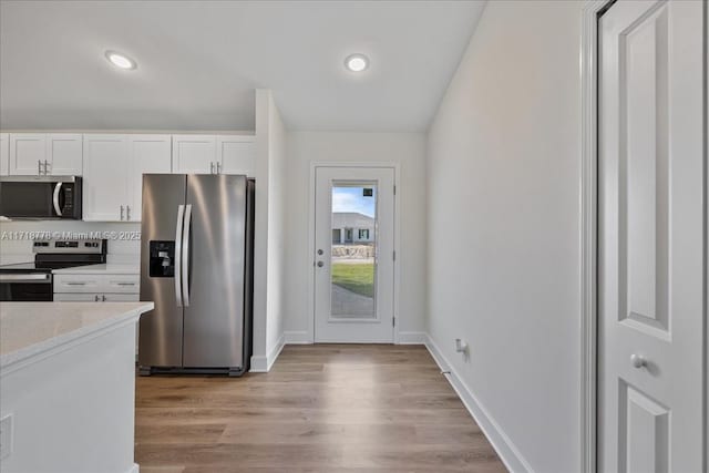 kitchen featuring light stone countertops, white cabinets, appliances with stainless steel finishes, and light hardwood / wood-style flooring