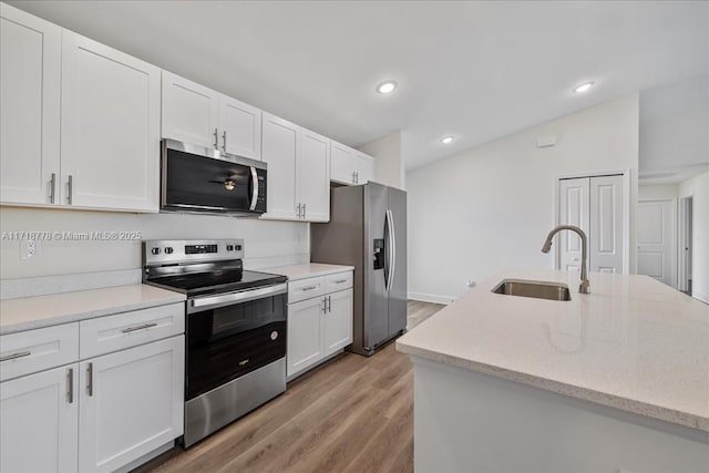 kitchen featuring light stone countertops, appliances with stainless steel finishes, white cabinetry, light hardwood / wood-style floors, and sink