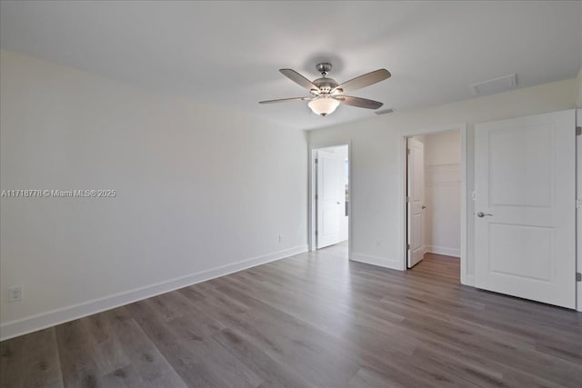 unfurnished bedroom with ceiling fan, a closet, a spacious closet, and dark hardwood / wood-style floors