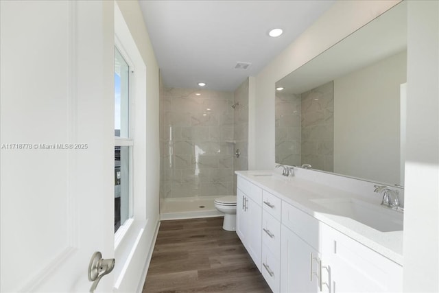 bathroom with toilet, vanity, a tile shower, and hardwood / wood-style flooring