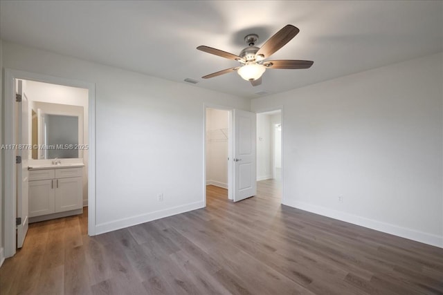 unfurnished bedroom with a spacious closet, a closet, light wood-type flooring, ceiling fan, and ensuite bathroom